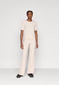 Μπλεζάκι μπεζ ριμπ πλεκτό με κολάρο και κοντά μανίκια, συνοδευόμενο από παντελόνι με φουσκωτή γραμμή και ίδια απόχρωση. Φορεμένο με μαύρα παπούτσια.