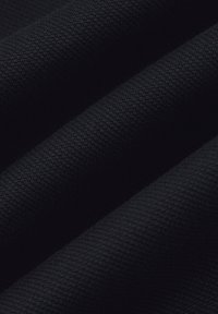 Czarna tkanina o teksturowanym splocie, z zagiętymi sekcjami, które tworzą głębię i subtelne cieniowanie. Powierzchnia jest gładka, a jednocześnie ustrukturyzowana.