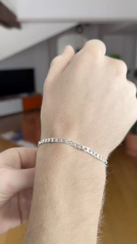 Strieborný náramok na ruke, ktorý tvorí prepojené oválne očká, hladká textúra a lesklý povrch.