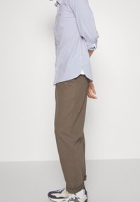 Chemise boutonnée rayée bleu clair avec des manches retroussées, associée à un pantalon ample marron et des baskets avec des accents bleus.