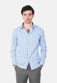 Camicia a righe blu e bianche con bottoni, maniche lunghe, colletto classico e vestibilità sagomata, abbinata a pantaloni grigi.
