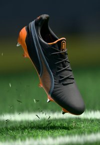 Scarpini da calcio neri e arancioni con tomaia testurizzata, forma allungata e sei tacchetti trasparenti; presenta il logo "KING" sulla linguetta.