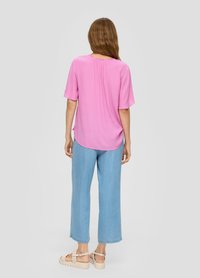 Roze t-shirt met korte mouwen en een relaxte pasvorm, afgeronde zoom en een plooien aan de achterkant, gecombineerd met lichtblauwe wijde broek en beige platform sandalen.
