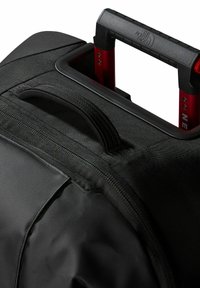 Borsa da viaggio nera in tessuto con un robusto manico telescopico rosso. Texture liscia con una zip e cuciture rinforzate sui bordi.