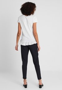 Top blanco de manga corta con un dobladillo con volantes, combinado con pantalones ajustados de rayas negras. El conjunto se complementa con zapatos de tacón cuadrado.