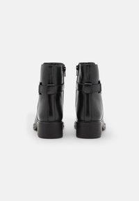 Bottines en cuir noir avec une finition lisse, des zips latéraux et un petit talon carré. Présente une sangle décorative et un détail de boucle.