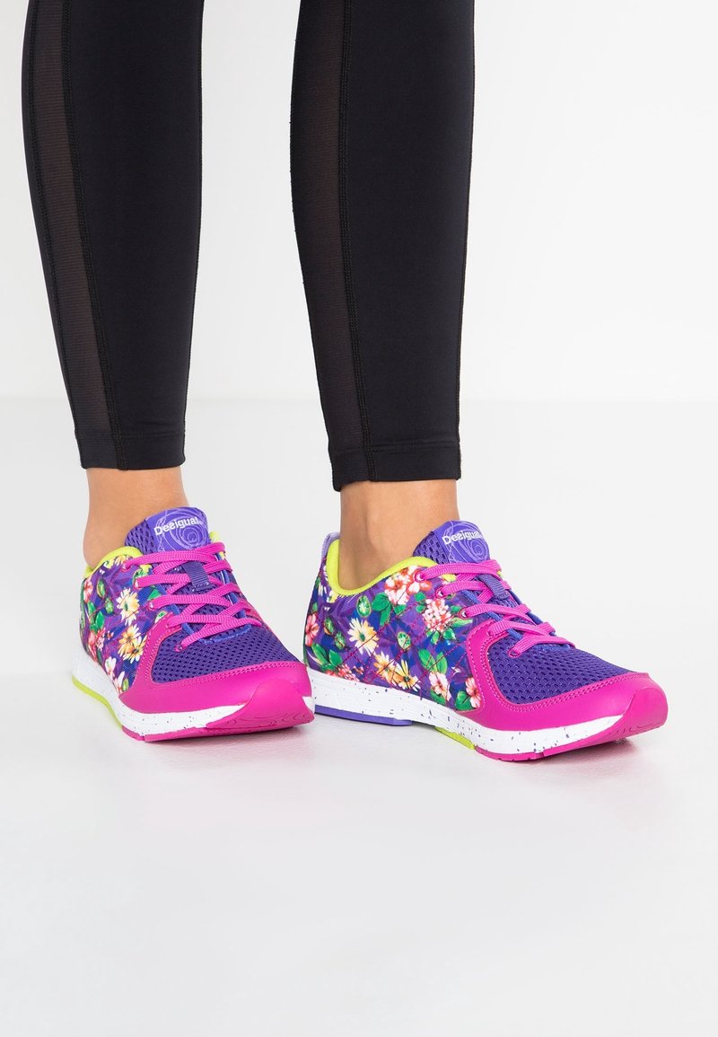 Baskets de sport florales avec une tige en maille violette, des accents rose vif et une semelle blanche mouchetée. Conception légère avec des détails texturés.