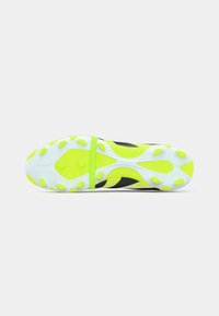 Semelle de chaussure de football avec des crampons blancs et jaune fluo sur un dessus noir et jaune, vue par le dessous sur un fond blanc.