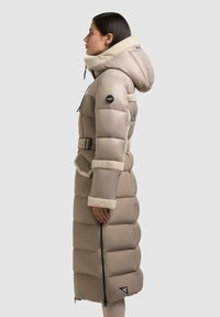 Piumino beige con cappuccio morbido, vita con cintura, zip laterale e accenti a contrasto in crema su polsini e colletto. Design fittamente trapuntato.