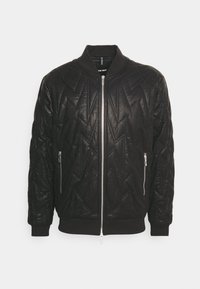 Veste bomber noire matelassée avec fermeture éclair à l'avant, poignets et ourlet côtelés, poches latérales zippées et un motif zigzag texturé sur l'ensemble.