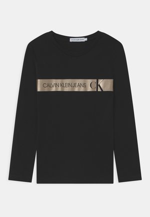 Schwarzes Langarmhemd aus Baumwolle, mit einem goldenen metallischen Streifen über der Brust, auf dem "CALVIN KLEIN JEANS" und das Logo prangen.