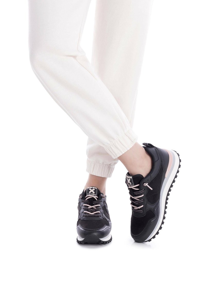 Zapatillas deportivas negras con acentos en rosa, materiales de ante texturizado y malla, con suela blanca contrastante y diseño de cordones.