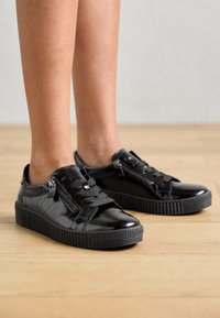 Sneaker in pelle verniciata nera con suole in gomma, lacci frontali e cerniere laterali. Presenta suole texturate e finitura liscia.