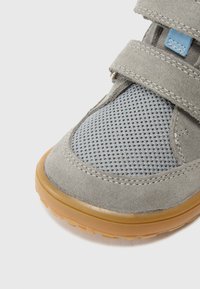 Grå ruskind og mesh-sneaker med justerbare velcro-stropper og en gummisål. Har en struktureret mesh-overdel for åndbarhed.