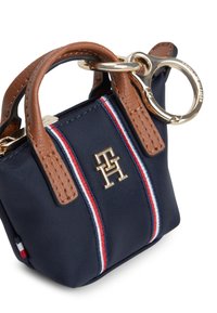 Τσάντα χειρός από ναυτικό ύφασμα με καφέ δερμάτινα χερούλια, διακοσμημένη με χρυσό τόνο λογότυπο και κόκκινες και λευκές ρίγες. Περιλαμβάνει κρικάκι για μπρελόκ.