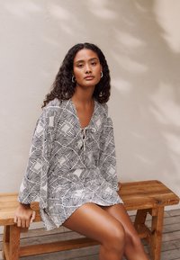 Black and white patterned dress with a V-neck and tie detail. Loose, lightweight fabric with long sleeves, featuring geometric designs.