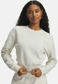 Sweatshirt crème, texturé, avec des poignets et une taille côtelés, arborant un petit détail brodé sur la poitrine. Coupe décontractée et confortable.