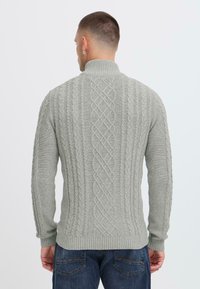 Gray knitted sweater featuring a high collar, cable knit pattern, ribbed cuffs, and hem. Worn with dark blue jeans.