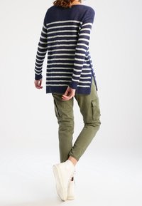 Marinblå och vit randig långärmad tröja med sidofickor, i kombination med olivgröna cargobyxor och vita sneakers.