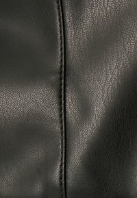 Zbliżenie na czarny materiał skórzany z widoczną, drobną fakturą i centralnym, pionowym szwem.