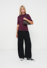 Un haut court à manches courtes bordeaux associé à un pantalon large noir. La tenue est complétée par un petit sac à main sombre et des baskets noires.