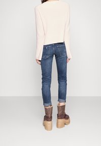 Ljusskär rosa kortärmad tröja med långa ärmar, tillsammans med mörkblå slim-fit jeans och bruna ankelstövlar med en rejäl sula.