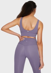 Ljubičasti sportski crop top i odgovarajuće tajice visokog struka, izrađene od rastezljivog materijala s glatkom teksturom i minimalnim detaljima brendiranja.