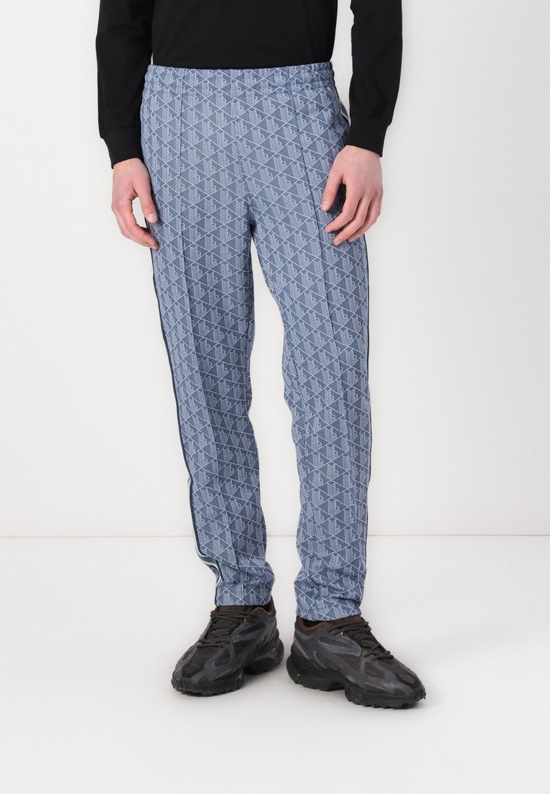 Blå mönstrade sweatpants med elastiskt midjeband, med en geometrisk design och sidostraper, tillsammans med svarta träningsskor.