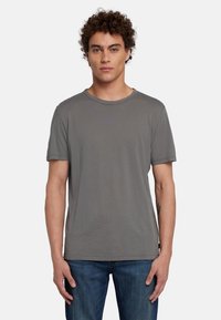 T-shirt grigia a maniche corte in morbido tessuto, con scollo rotondo e vestibilità rilassata. Indossata con jeans in denim blu.