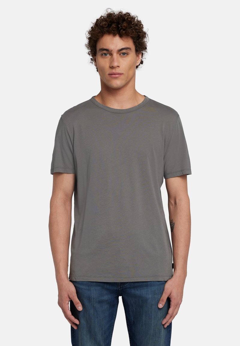 T-shirt grigia a maniche corte in morbido tessuto, con scollo rotondo e vestibilità rilassata. Indossata con jeans in denim blu.