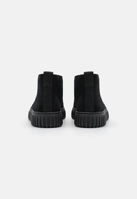 Stivaletti alla caviglia in suede nero con pannelli laterali elasticizzati, punta arrotondata e suola in gomma testurizzata con scanalature. Design minimalista.