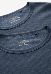 Dva tamnoplava termalna majica s okruglim izrezom, teksturiranom tkaninom i oznakama koje prikazuju "NEXT THERMOGEN M" i "MADE IN BANGLADESH".