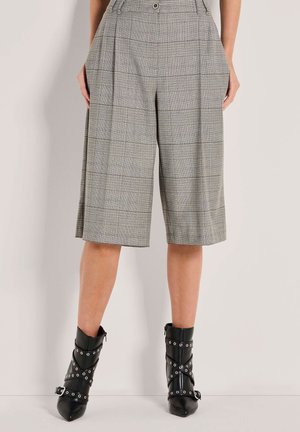 Person, der knielange graue kariert Culottes und schwarze spitze Ankle Boots mit Schnallen- und Riemendetails trägt.
