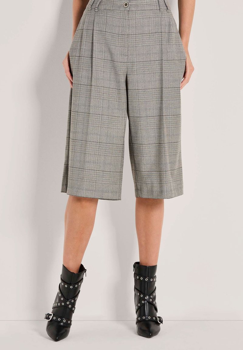 Person, der knielange graue kariert Culottes und schwarze spitze Ankle Boots mit Schnallen- und Riemendetails trägt.