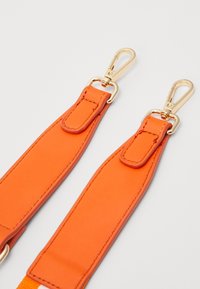 Orange syntetisk rem med guldfärgad hårdvara, med slät textur och rundade ändar, designad för att fästa vid väskor eller liknande föremål.