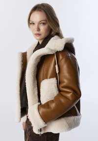 Bruine leren jas met een faux fur binnenvoering en kraag, voorzien van een voorzak, ritssluiting en verstelbaar trekkoorddetail.