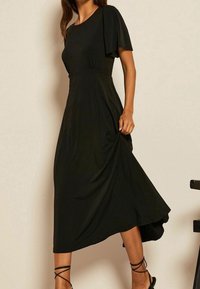 Mustat midi-mekko, jossa on pyöreä pääntie, lyhyet liehuvat hihat ja rypistetty vyötäröyksityiskohta. Valmistettu sileästä, virtaavasta kankaasta.