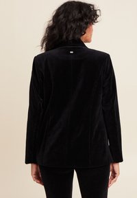 Blazer in corduroy nero con superficie testurizzata. Taglio originale con colletto a scollatura a V e piccola etichetta con marchio sul retro, maniche lunghe.
