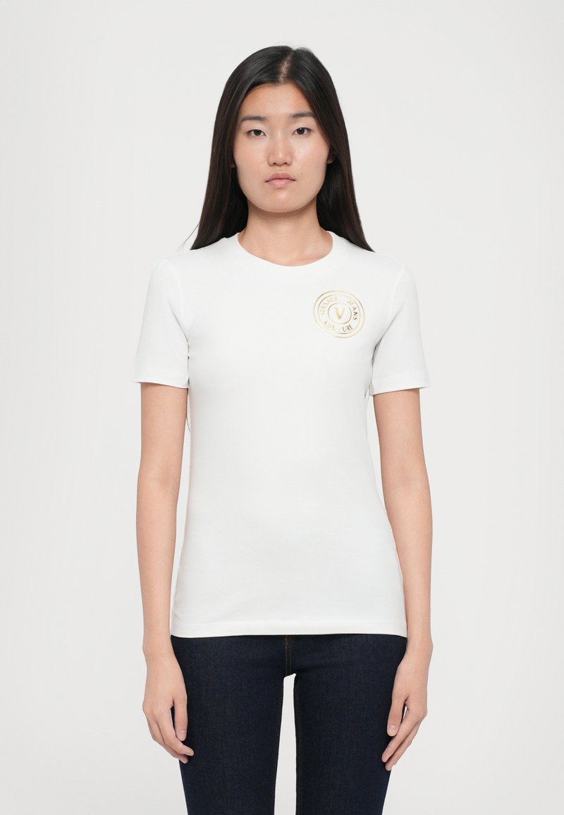 T-shirt branco de manga curta feito de algodão suave com um decote redondo, apresentando um logotipo redondo dourado na área do peito esquerdo.
