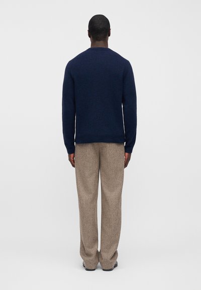 Σκούρο μπλε πουλόβερ πλεκτό με στρογγυλή λαιμόκοψη και μακριά μανίκια, συνδυασμένο με ανοιχτό καφέ, φαρδιά υφασμάτινη παντελόνια με υφή. Το σύνολο έχει άνετη εφαρμογή.