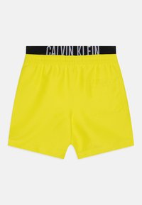 Žute kupaće hlače s crnim elastičnim pojasom na kojem se nalazi logo "CALVIN KLEIN". Dovršene s jednim stražnjim džepom i glatkom teksturom.