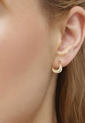 Close-up af en kvindes øre med en lille, glat, skinnende guldring på lyshud og blondt hår.