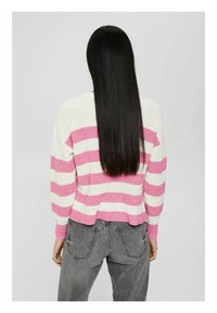 Persona con cabello largo y lacio negro, vistiendo un suéter a rayas blanco y rosa y jeans grises, vista desde atrás.