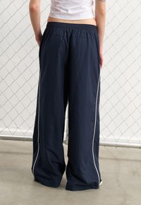 Pantalons larges bleu marine en matériau léger, dotés d'une bande latérale blanche et d'une taille élastique pour un ajustement décontracté.