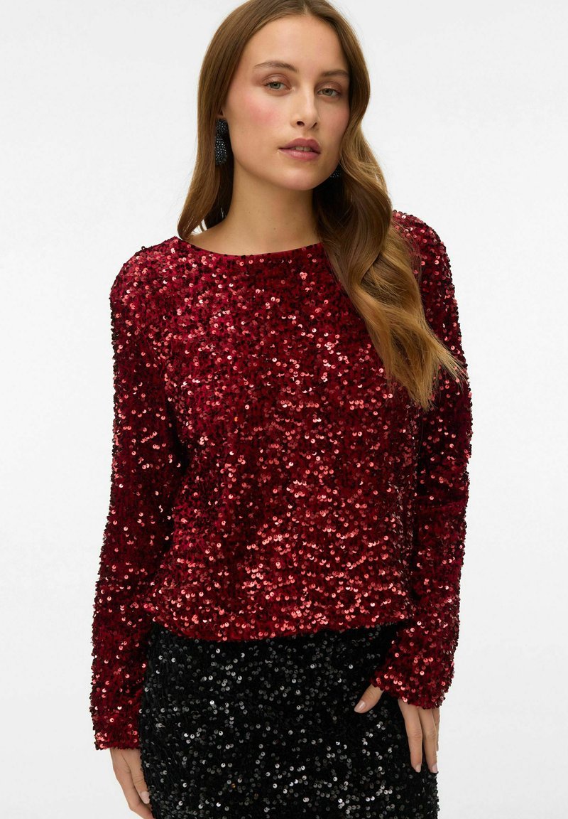 Rød pailletbluse med lange ærmer, rund halsudskæring og løs pasform. Teksturen er blank med forskellige nuancer af røde palietter over det hele.