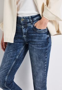 Jeans in denim blu scuro con accenti sbiaditi, design a cinque tasche e hardware argentato. Il tessuto è morbido con una superficie liscia.