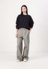 Fekete crewneck pulóver domború felirattal, világosszürke cargo nadrággal párosítva, oldalsó zsebekkel és rugalmas derékbőséggel. Hétköznapi cipők.