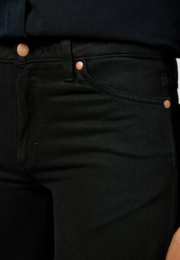 Black denim jeans with a fitted design. Copper button accents and subtle texture. Features a classic five-pocket layout.