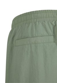 Zöld, könnyű anyagú rövidnadrág elasztikus derékkal és egyetlen, fedeles hátsó zsebbel. Simá szövet és minimalista dizájn.