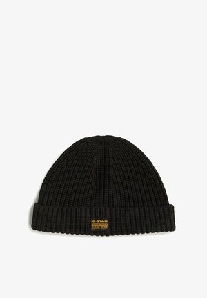 Zwarte gebreide beanie muts met een geribbelde textuur en omgeslagen rand. Bevat een kleine gele en zwarte logopatch aan de voorkant.